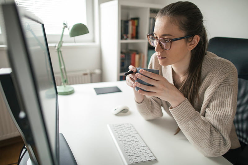 home-office-mais-produtivo-contraktor Mulher tomando café, em frente ao computador, em home office